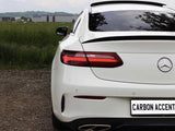 A white Mercedes-Benz car is parked on gravel, facing away. The license plate reads 