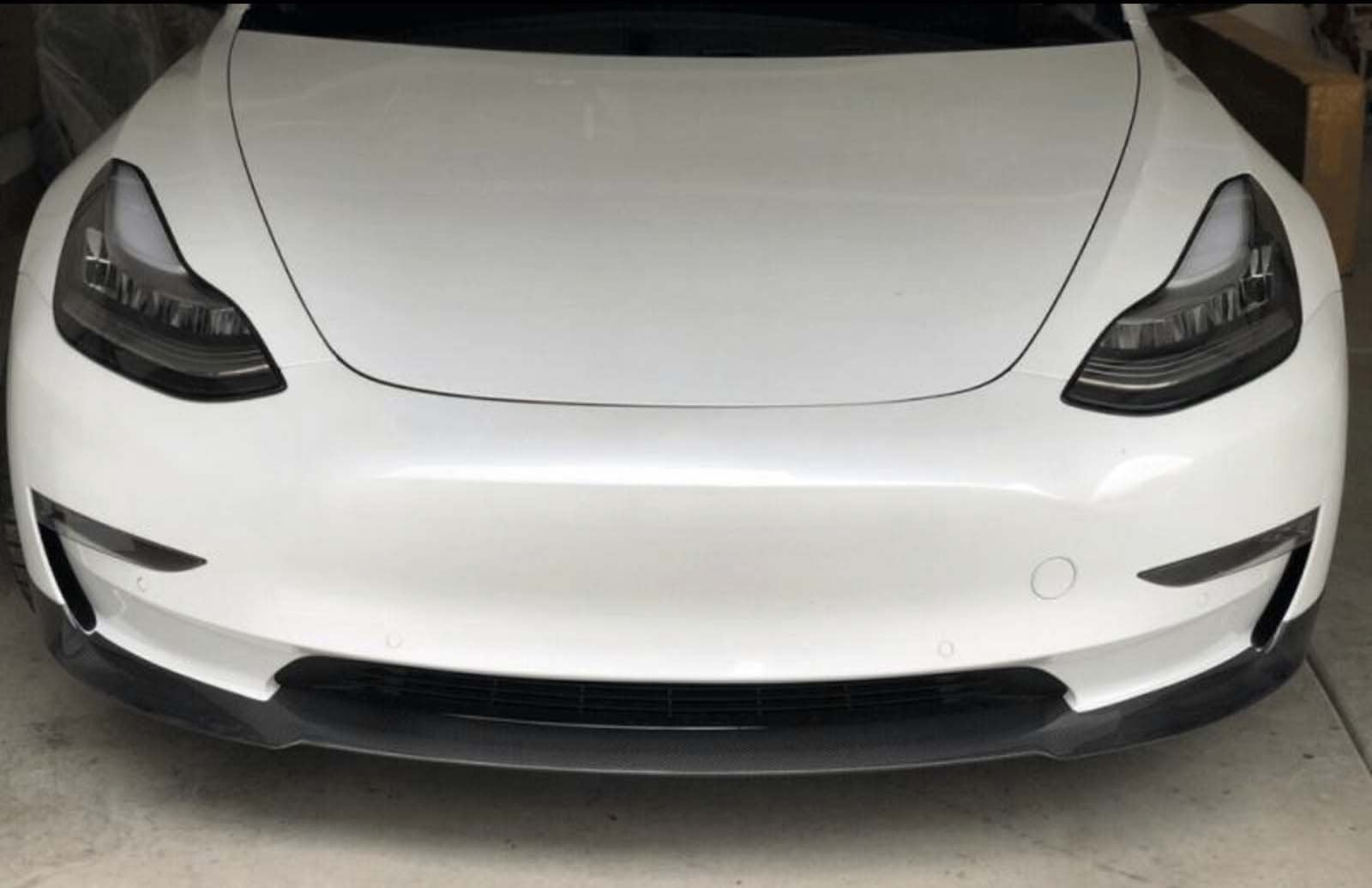 A white car is parked in a garage, focusing on its sleek front design with prominent headlamps and a smooth bumper.