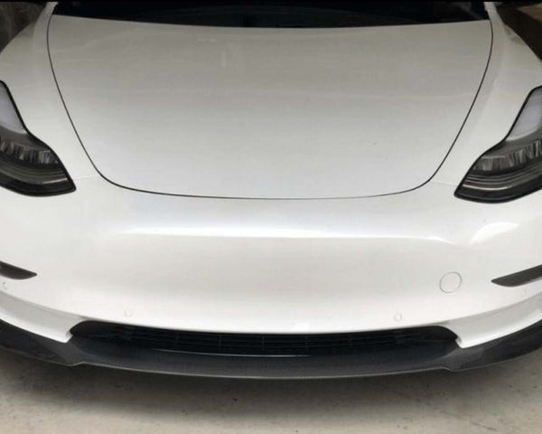 A white car is parked in a garage, focusing on its sleek front design with prominent headlamps and a smooth bumper.