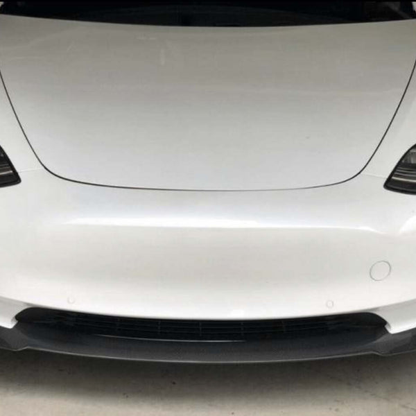 A white car is parked in a garage, focusing on its sleek front design with prominent headlamps and a smooth bumper.
