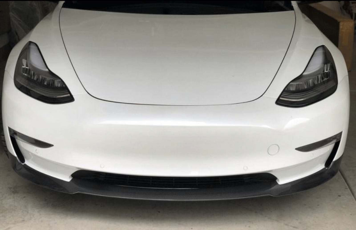 A white car is parked in a garage, focusing on its sleek front design with prominent headlamps and a smooth bumper.