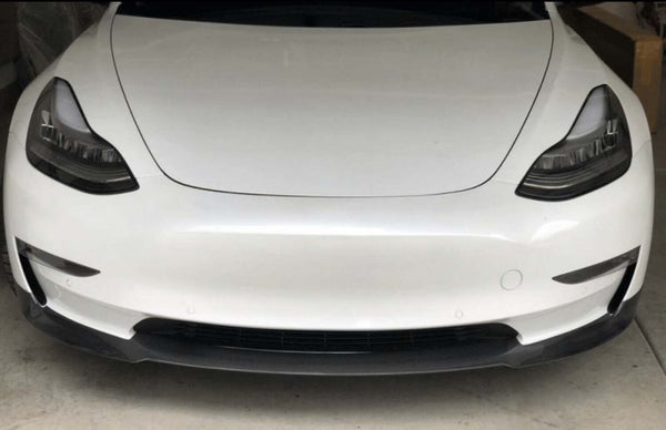 A white car is parked in a garage, focusing on its sleek front design with prominent headlamps and a smooth bumper.
