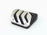 A metal car pedal features three black grooves and a black rubber edge, resting on a white background.