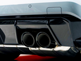 Dual exhaust pipes, surrounded by a carbon fiber diffuser, protrude from the rear of a sleek white car, emphasizing a sporty, high-performance design in an indoor setting.