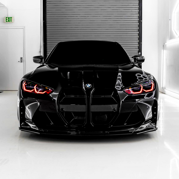 A sleek black car with illuminated red headlights is parked in a well-lit garage. The garage has a closed metal shutter and a visible "EXIT" sign on the left wall.