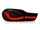 A sleek, smoked car taillight illuminates brightly with red LED lights in an elegant pattern, set against a plain white background.