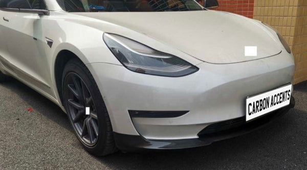 White car with sleek design parked beside brick wall; "CARBON ACCENTS" text on license plate; black rims and tinted windows complete its modern appearance.