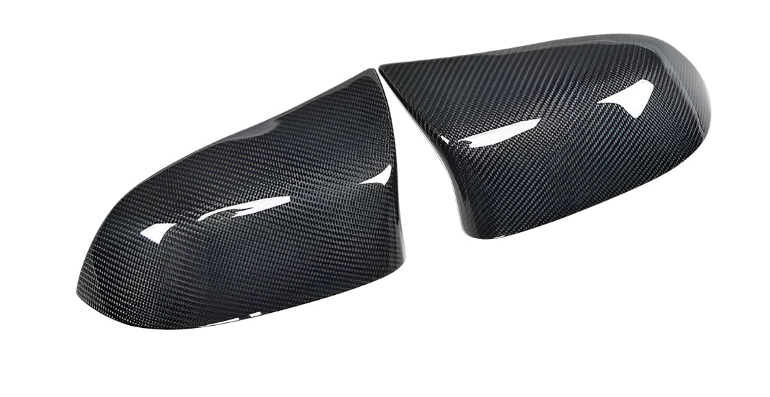 Two carbon fiber car mirror covers are positioned side by side, reflecting light. They have a sleek, shiny surface against a plain white background, indicating a modern automotive design.