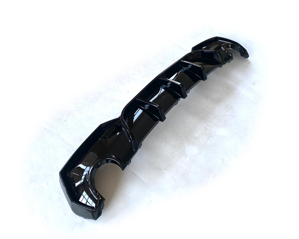 A glossy black car diffuser with several fins lies on a white surface, designed for aerodynamic enhancement.