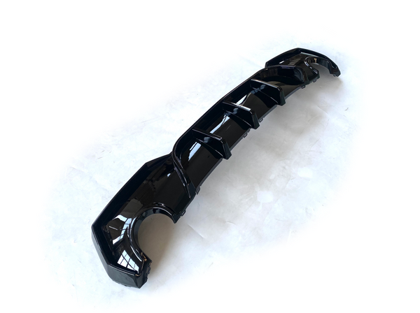 A glossy black car diffuser with several fins lies on a white surface, designed for aerodynamic enhancement.