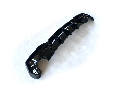 A glossy black car diffuser with several fins lies on a white surface, designed for aerodynamic enhancement.