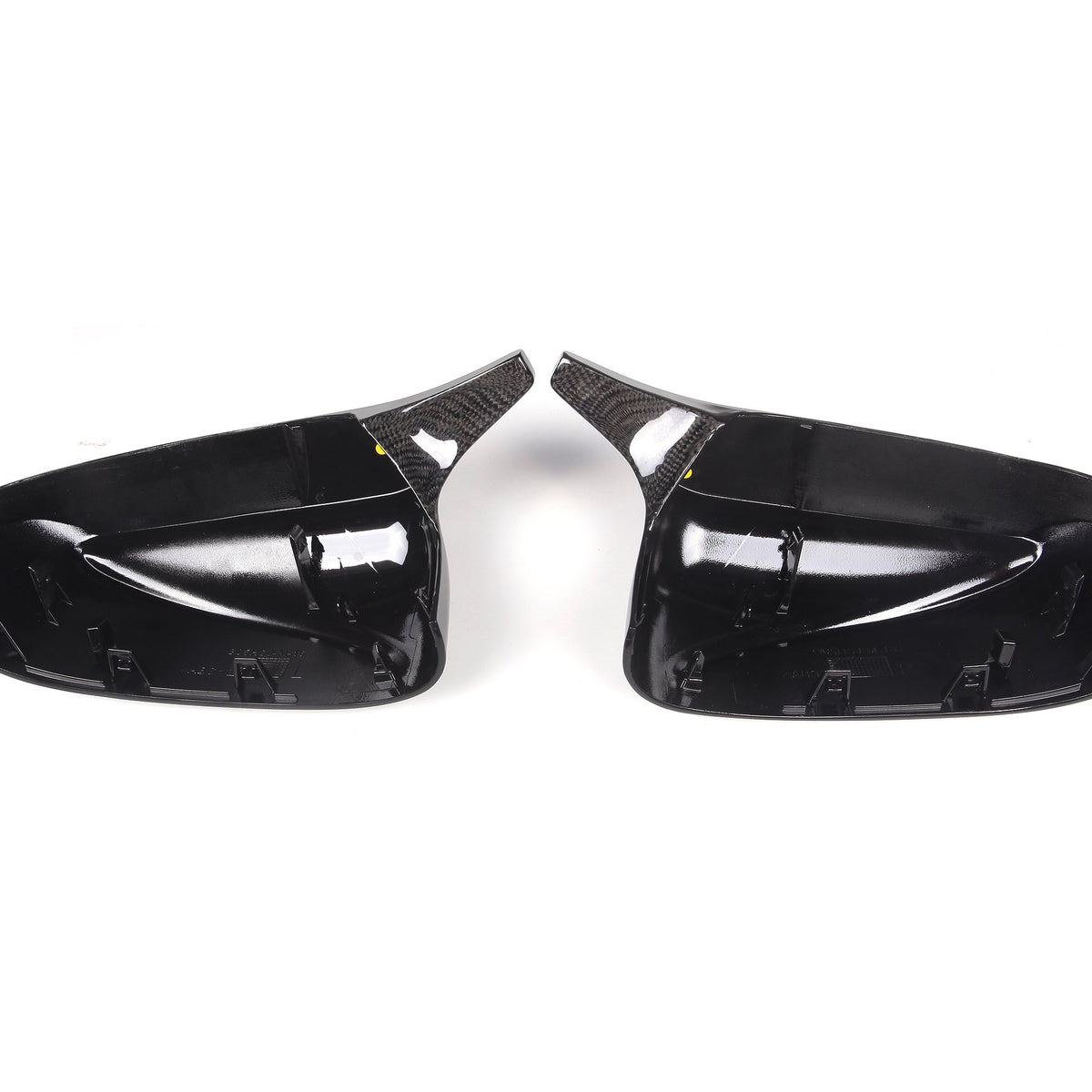 Two black, glossy car side mirror covers face each other, highlighting their contoured interior and carbon fiber textures, set against a plain white background.