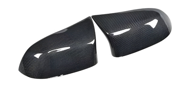Two carbon fiber mirror covers rest side by side, reflecting light on their glossy surface, set against a plain white background.