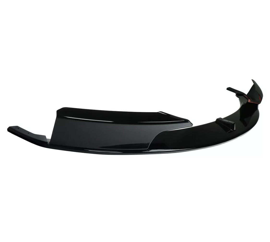A glossy black car bumper lip rests against a white background, showcasing its aerodynamic design with sharp edges and smooth curves.