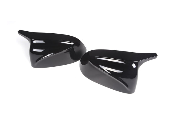 Two glossy black car side mirror covers lie on a blank white surface, each with a sleek, aerodynamic design featuring smooth, curved lines.