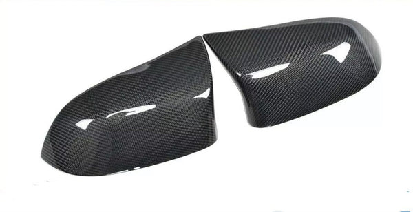 Two glossy carbon fiber car mirror covers rest on a white surface, reflecting light and showcasing their textured pattern.