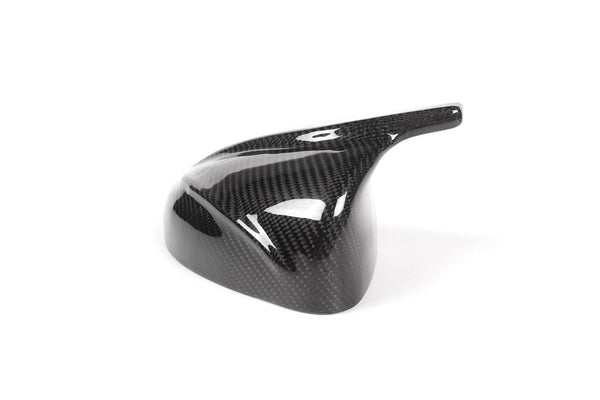 A glossy, black carbon fiber vehicle mirror cover is placed on a plain white background, showcasing its sleek, aerodynamic design and lightweight material.