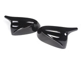 Two glossy black side mirror covers reflect light, positioned on a white background. The covers have a sleek, aerodynamic design, suggesting use for a vehicle.