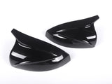 Two sleek, black, aerodynamic car mirror covers lay side by side on a plain white background, emphasizing their glossy finish and curved design.