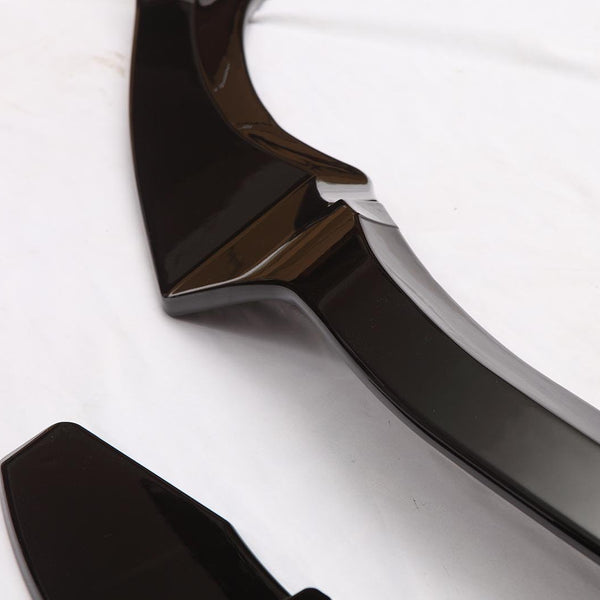 A glossy black automotive trim piece lies on a white surface, featuring smooth, angular shapes and reflective curves, suggesting a component for vehicle customization or aesthetics.