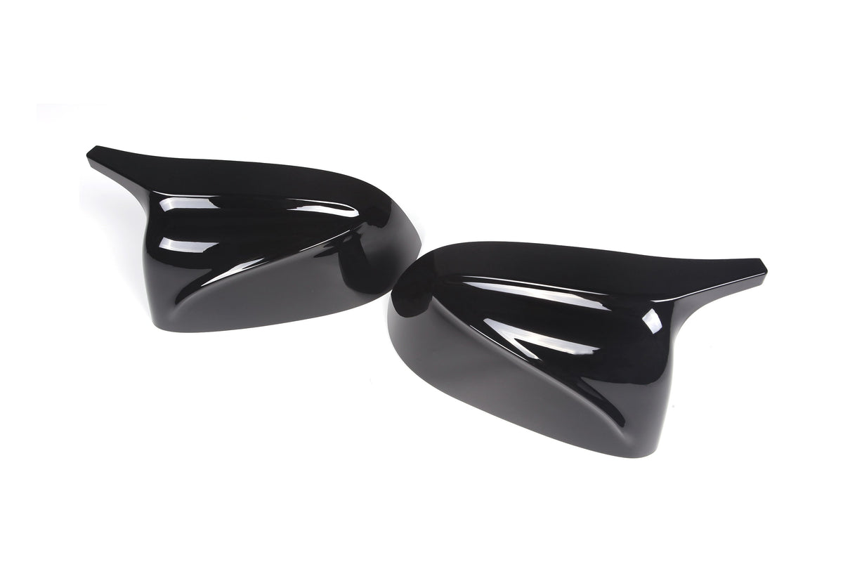 Two glossy, black car side mirror covers lie side by side on a plain white background, showcasing a sleek and aerodynamic design.
