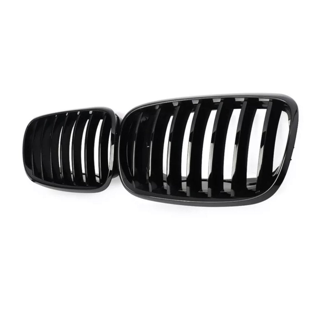 Black car grilles rest side by side, featuring vertical slats. They are showcased against a plain white background, highlighting their shiny, smooth finish.