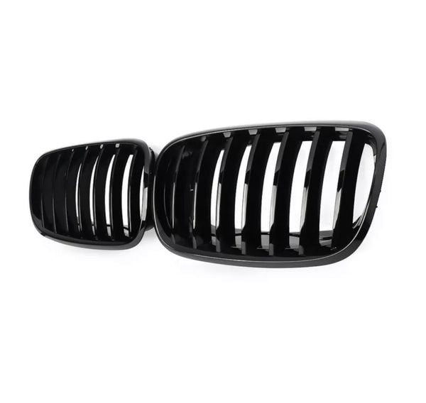 Black car grilles rest side by side, featuring vertical slats. They are showcased against a plain white background, highlighting their shiny, smooth finish.