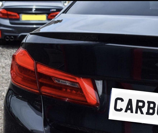 A black car's rear with bright red taillights is parked in a gravel area. The license plate reads "CARBON." Another vehicle is visible in the background.