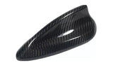 Carbon fiber car mirror cover; sleek and glossy, with a textured, woven pattern reflecting light. The cover rests against a plain white background, emphasizing its aerodynamic design.