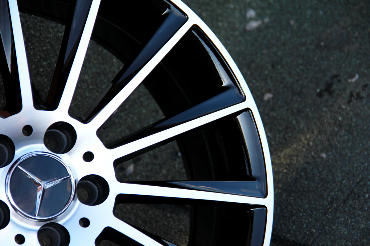 A black and silver alloy wheel with a star emblem is stationary on a rough, gray concrete surface.