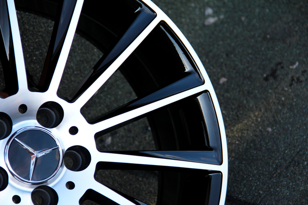 A black and silver alloy wheel with a star emblem is stationary on a rough, gray concrete surface.