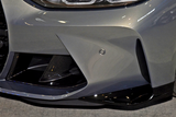 The gray car bumper features sleek, aerodynamic vents and a small sensor, situated on a reflective showroom floor with overhead lighting.