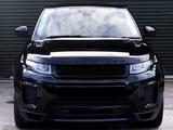 A black Range Rover stands stationary, facing forward, on concrete ground against a closed, corrugated metal door. The vehicle's headlights and grill are prominent. Text on the hood: 