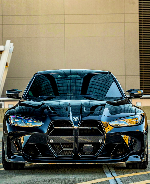 A sleek black car is stationary on a rooftop parking lot. Its modern design features aggressive front grilles and sharp headlights, with a reflective glass building visible in the background.