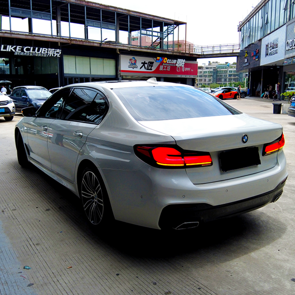 A silver sedan, parked, in an urban setting with adjacent shops and cars. Prominent signage above the shops includes "LIKE CLUB" and other Chinese text.