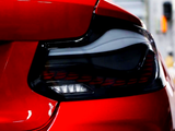 A shiny red car's taillight is prominently featured, with sleek, modern contours in a brightly lit garage setting.