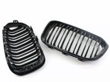 Two black car grille parts, each with parallel vertical slats, are positioned side by side. They are set against a plain, white background.
