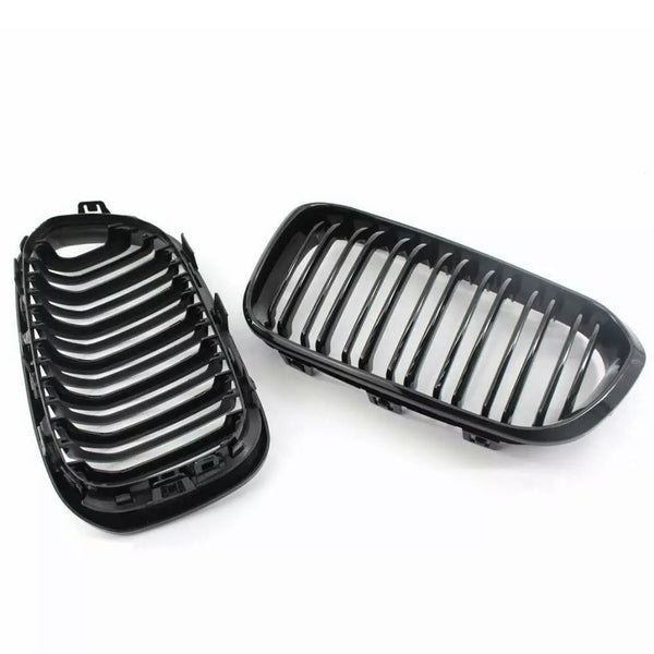 Two black car grille parts, each with parallel vertical slats, are positioned side by side. They are set against a plain, white background.