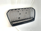 A black hexagonal mesh car grille rests against a white background. The grille features a honeycomb pattern and two round mounting points, suggesting automotive use.
