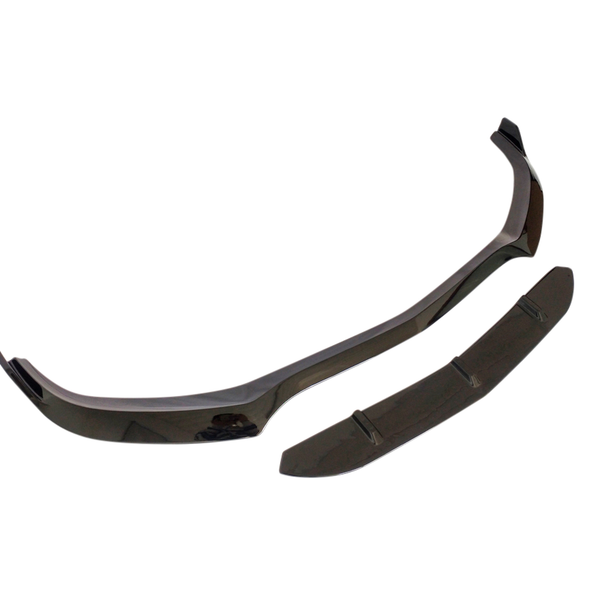A black car front splitter lies against a white background, consisting of two separate aerodynamic pieces designed to improve vehicle stability and reduce drag.