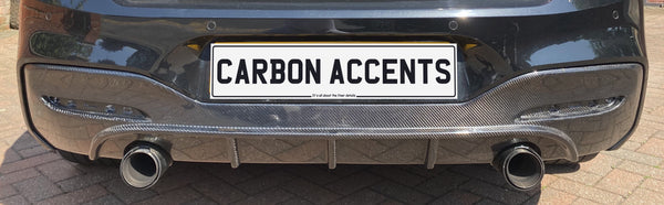 Car rear end with dual exhaust pipes, carbon fiber diffuser, and a license plate reading "CARBON ACCENTS." It’s parked on a brick driveway.