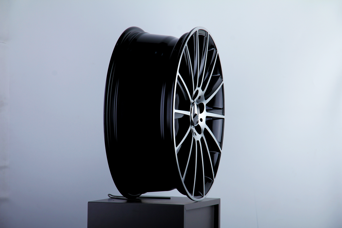 A sleek, black car wheel rim with intricate, multi-spoke design stands upright on a pedestal against a plain, light background.