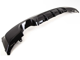 A glossy black car bumper diffuser with fins lies on a plain white background, showcasing its aerodynamic contours and smooth finish.