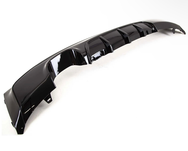 A glossy black car bumper diffuser with fins lies on a plain white background, showcasing its aerodynamic contours and smooth finish.