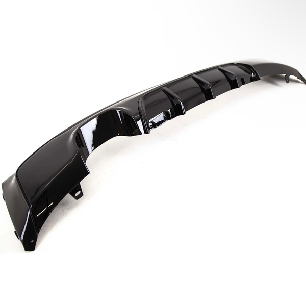 A glossy black car bumper diffuser with fins lies on a plain white background, showcasing its aerodynamic contours and smooth finish.