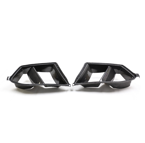 Carbon fiber car exhaust tips with dual openings, facing each other on a plain white background.