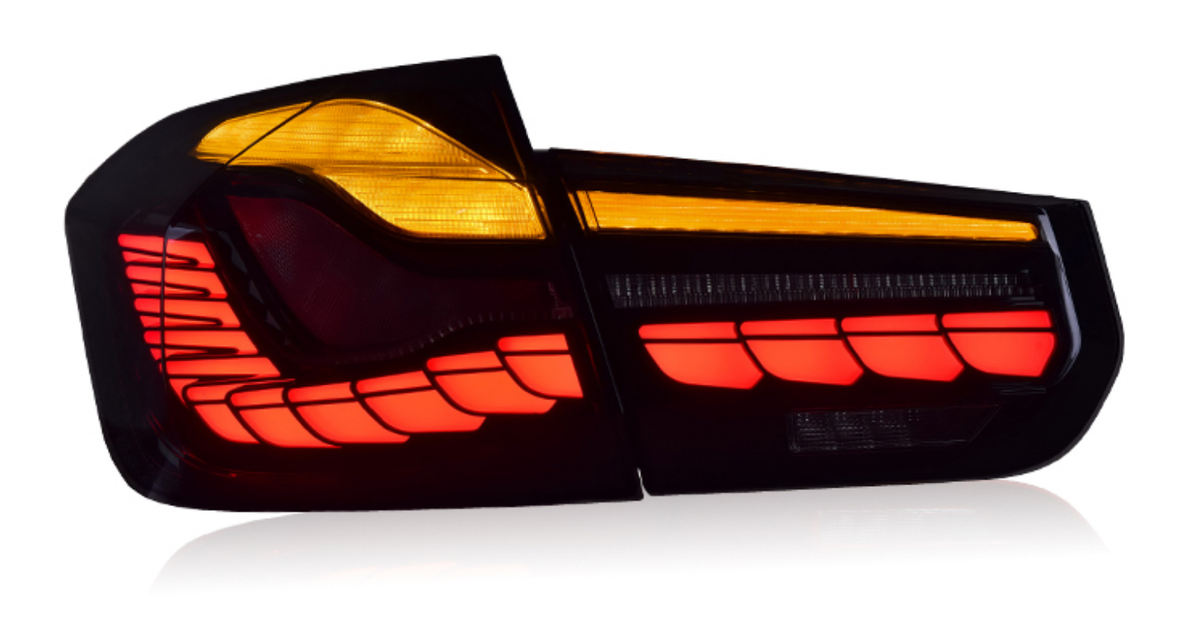 Car taillight illuminated, displaying bright red and amber segments. Positioned against a plain white background, the light consists of modern, geometric shapes, providing a sleek, stylish appearance.