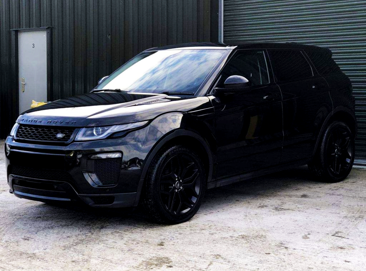 A black Range Rover parked on a concrete surface beside a dark corrugated metal building with a closed door labeled "3."