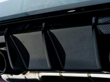 Carbon fiber rear diffuser with three vertical fins, flanked by metallic exhaust pipes, is mounted under a car's bumper in a well-lit garage setting.