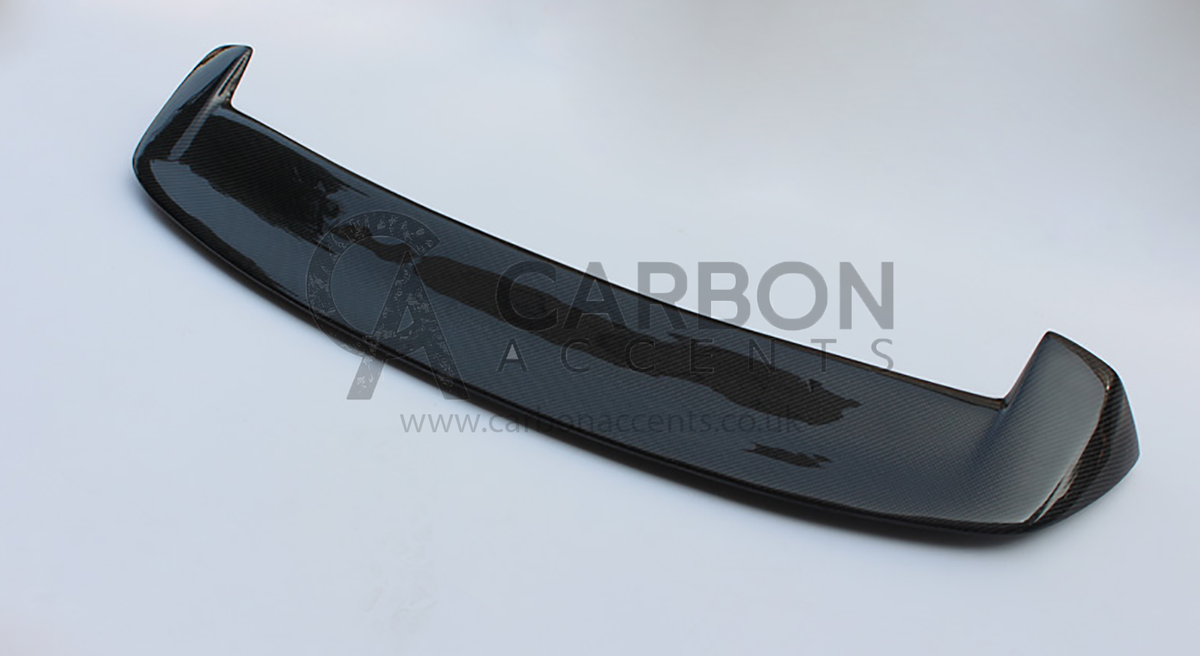 A black carbon fiber car spoiler with a sleek design rests on a plain white background. Text: "CARBON ACCENTS" and "www.carbonaccents.com".